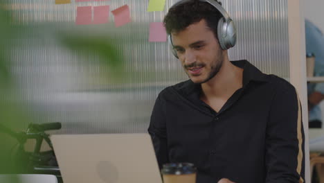 attractive-young-hispanic-man-student-using-laptop-computer-listening-to-music-working-friendly-colleague-sharing-juice-showing-support-in-happy-multi-ethnic-office