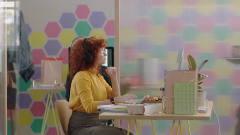 beautiful-young-redhead-business-woman-using-computer-brainstorming-working-on-creative-project-in-colorful-modern-office-listening-to-music-wearing-headphones