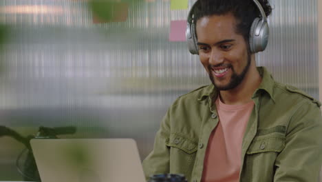 attractive-young-mixed-race-man-student-using-laptop-computer-watching-online-entertainment-smiling-enjoying-listening-to-music-in-office