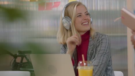 beautiful-young-caucasian-business-woman-using-laptop-computer-listening-to-music-working-friendly-colleague-sharing-juice-showing-support-in-happy-multi-ethnic-office