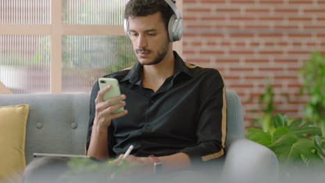 young-hispanic-man-using-digital-tablet-computer-drawing-browsing-online-sharing-social-media-messages-student-sketching-enjoying-listening-to-music-checking-smartphone-in-modern-office