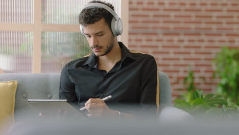 young-hispanic-man-using-digital-tablet-computer-drawing-browsing-online-sharing-social-media-messages-student-sketching-enjoying-listening-to-music-in-modern-office