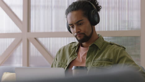 young-mixed-race-man-using-laptop-computer-browsing-online-messages-sharing-network-communication-student-drinking-coffee-enjoying-listening-to-music-in-modern-office