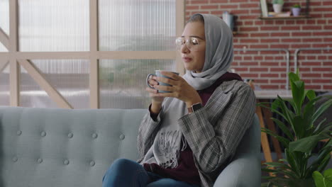 Schöne-Muslimische-Geschäftsfrau,-Die-Kaffee-Trinkt,-Indem-Sie-Ihr-Smartphone-Nutzt,-Um-Social-Media-Nachrichten-Zu-Durchsuchen-Und-SMS-Zu-Schreiben,-Die-Erfolgreiche-Karriereideen-Teilen-Und-Ein-Hijab-Kopftuch-An-Einem-Modernen-Büroarbeitsplatz-Tragen