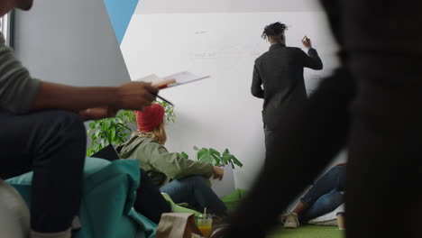 young-african-american-businesman-teaching-group-of-students-showing-project-timeline-on-whiteboard-presenting-graph-data-diverse-team-brainstorming-sharing-ideas-in-office-lecture