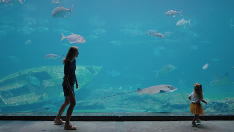mother-with-daughter-at-aquarium-looking-at-beautiful-fish-swimming-in-tank-little-girl-observing-marine-animals-with-curiosity-having-fun-learning-about-marine-life-with-mom-in-oceanarium