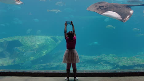 Kleines-Mädchen-Fotografiert-Fische-Im-Aquarium-Mit-Dem-Smartphone,-Fotografiert-Meerestiere,-Die-Im-Becken-Schwimmen,-Lernt-Etwas-über-Das-Leben-Im-Meer-Im-Wasserlebensraum-Und-Hat-Spaß-Im-Ozeanarium