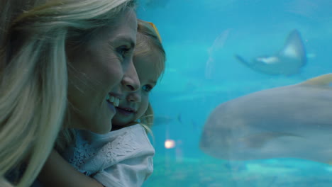 Glückliche-Mutter-Mit-Tochter-Im-Aquarium-Und-Blick-Auf-Wunderschöne-Fische,-Die-Im-Aquarium-Schwimmen.-Kleines-Mädchen-Beobachtet-Neugierig-Meerestiere-Und-Hat-Spaß-Daran,-Mit-Ihrer-Mutter-Im-Ozeanarium-Etwas-über-Das-Leben-Im-Meer-Zu-Lernen