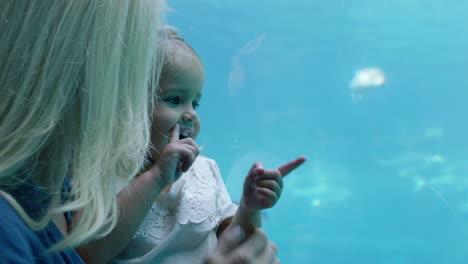 Glückliches-Mädchen-Mit-Mutter-Im-Aquarium-Und-Blick-Auf-Schöne-Fische,-Die-Im-Aquarium-Schwimmen.-Kind-Beobachtet-Neugierig-Meerestiere-Und-Hat-Spaß-Daran,-Mit-Mutter-Im-Ozeanarium-Etwas-über-Das-Leben-Im-Meer-Zu-Lernen