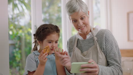 Großmutter-Und-Kind-Nutzen-Smartphone-Beim-Videochat.-Kleines-Mädchen-Teilt-Urlaubswochenende-Und-Zeigt-Kekse-Mit-Oma,-Die-Es-Genießt,-Zu-Hause-Mit-Ihrer-Enkelin-Auf-Dem-Handy-Zu-Chatten