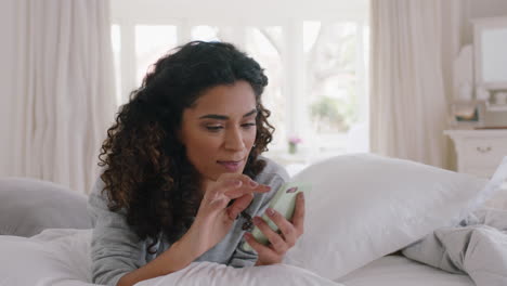 young-beautiful-woman-using-smartphone-texting-browsing-social-media-messages-enjoying-mobile-phone-communication-lying-on-bed-at-home-4k-footage