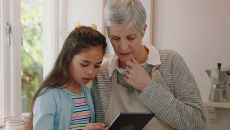 Süßes-Kleines-Mädchen,-Das-Der-Großmutter-Zeigt,-Wie-Man-Einen-Tablet-Computer-Benutzt,-Und-Der-Oma-Moderne-Technologie-Beibringt,-Intelligentes-Kind,-Das-Der-Oma-Zu-Hause-Mit-Einem-Mobilen-Gerät-Hilft