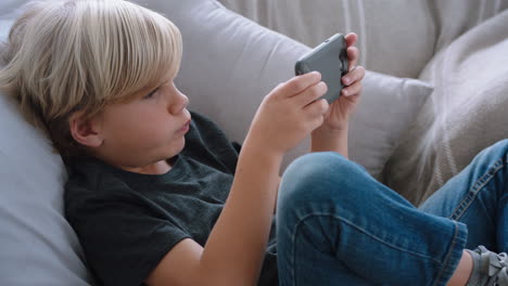 Fröhlicher-Kleiner-Junge,-Der-Sein-Smartphone-Benutzt-Und-Ein-Spiel-Spielt,-Das-Sich-Zu-Hause-Auf-Dem-Sofa-Entspannt.-Kind,-Das-Online-Mit-Mobiltelefontechnologie-Surft,-Anti-Social-Sucht-Konzept,-4K-Videos