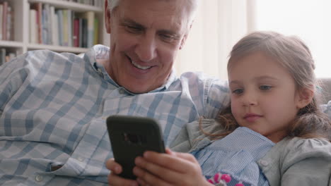 Glücklicher-Großvater-Zeigt-Kleinem-Mädchen,-Wie-Man-Das-Smartphone-Benutzt,-Und-Lehrt-Neugierige-Enkelin-Moderne-Technologie.-Intelligentes-Kind-Lernt-Mobiltelefon,-Das-Mit-Opa-Auf-Dem-Sofa-Sitzt