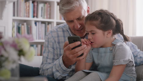 Großvater-Zeigt-Süßem-Kleinen-Mädchen,-Wie-Man-Ein-Smartphone-Benutzt,-Und-Lehrt-Neugierige-Enkelin,-Moderne-Technologie,-Intelligentes-Kind,-Das-Mobiltelefon-Lernt,-Sitzt-Mit-Opa-Auf-Dem-Sofa