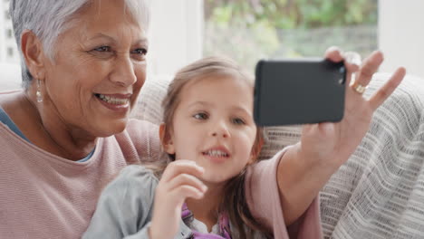 Kleines-Mädchen-Nutzt-Smartphone-Mit-Großmutter-Beim-Videochat,-Winkt-Der-Familie-Zu-Und-Teilt-Ihr-Urlaubswochenende-Mit-Oma,-Die-Auf-Dem-Handy-Chattet-Und-Sich-Zu-Hause-Mit-Enkelin-In-4k-Entspannt