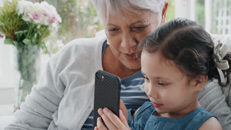 Entzückendes-Kleines-Mädchen,-Das-Großmutter-Zeigt,-Wie-Man-Ein-Smartphone-Benutzt,-Und-Oma-Moderne-Technologie-Beibringt,-Intelligentes-Kind,-Das-Oma-Mit-Dem-Mobiltelefon-Zu-Hause-Hilft,-4K