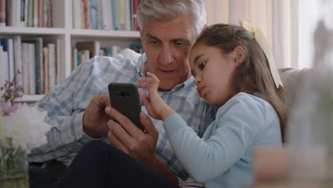 Großvater-Zeigt-Süßem-Kleinen-Mädchen,-Wie-Man-Ein-Smartphone-Benutzt,-Und-Lehrt-Neugierige-Enkelin,-Moderne-Technologie,-Intelligentes-Kind,-Das-Mobiltelefon-Lernt,-Sitzt-Mit-Opa-Auf-Dem-Sofa