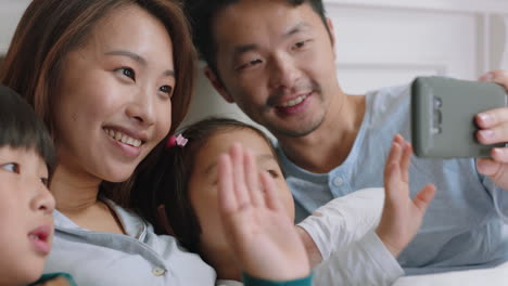 Glückliche-Asiatische-Familie-Beim-Video-Chat-Mit-Dem-Smartphone-Im-Bett.-Mutter-Und-Vater-Mit-Kindern-Winken,-Chatten-Mit-Freunden-Auf-Dem-Mobiltelefon-Und-Genießen-Online-Kommunikation-In-4K-Videos