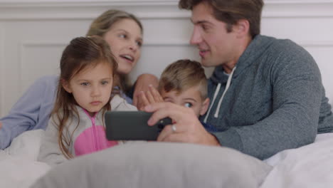 Glückliche-Familie-Mit-Smartphone-Im-Bett,-Mutter-Und-Vater-Mit-Kindern,-Die-Sich-Unterhaltung-Beim-Spielen-Auf-Dem-Handy-Ansehen-Und-Am-Wochenendmorgen-Gemeinsam-Spaß-Haben,-4K-Videos