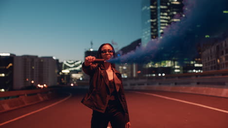 young-woman-holding-blue-smoke-bomb-in-city-at-night