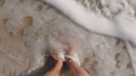 top-view-waves-gently-splashing-feet-woman-standing-barefoot-on-beach-enjoying-summer-vacation
