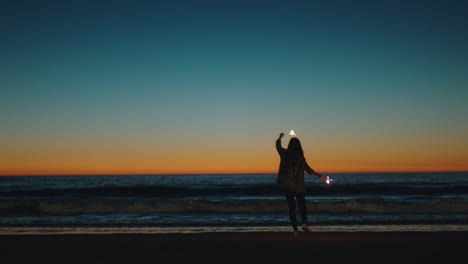 girl-dancing-with-sparklers-on-beach-at-sunset-celebrating-new-years-eve-woman-having-fun-dance-with-sparkler-fireworks-enjoying-independence-day-celebration-by-the-sea