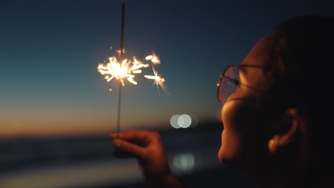 portrait-mixed-race-girl-holding-sparkler-on-beach-at-sunset-celebrating-new-years-eve-young-woman-enjoying--independence-day-celebration-4th-of-july
