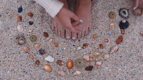 Nahaufnahme-Der-Füße-Einer-Frau,-Die-Muscheln-Am-Strand-Sammelt-Und-Die-Wunderschöne-Natürliche-Vielfalt-Genießt,-Die-Muster-Auf-Sand-Formt