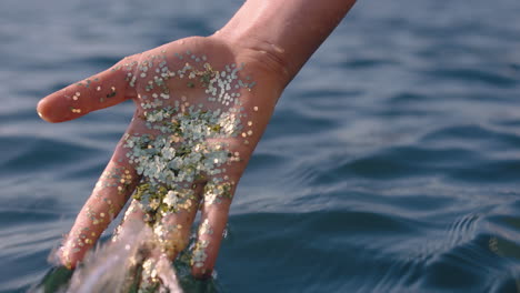 close-up-hand-holding-glitter-touching-sea-water-splashing-creative-art-concept