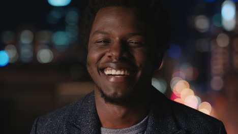 Retrato-De-Un-Apuesto-Hombre-Afroamericano-En-La-Azotea-Por-La-Noche-Sonriendo-Feliz-Disfrutando-De-La-Vida-Nocturna-Urbana-Con-Luces-Bokeh-De-La-Ciudad-En-El-Fondo