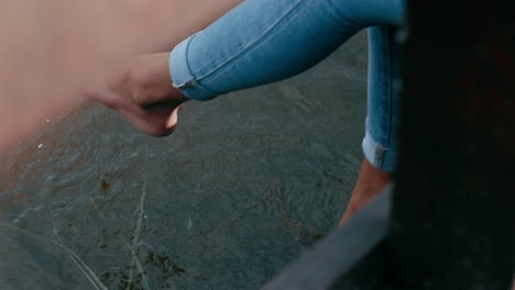 close-up-woman-legs-dangling-over-water-young-girl-enjoying-time-alone-sitting-on-wooden-bridge-in-park