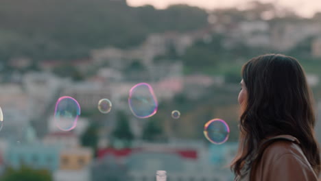 beautiful-young-caucasian-woman-blowing-bubbles-on-rooftop-at-sunset-enjoying-playful-summer-day-with-city-in-background