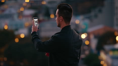 young-man-using-smartphone-taking-photo-of-beautiful-city-skyline-enjoying-rooftop-view-at-sunset-sharing-vacation-travel-photography-on-social-media