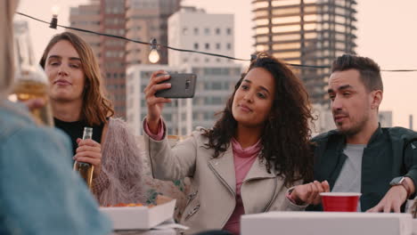 happy-multi-ethnic-friends-enjoying-weekend-rooftop-party-drinking-taking-selfie-photos-using-smartphone-sharing-on-social-media