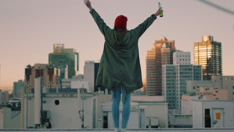 happy-young-woman-walking-on-rooftop-with-arms-raised-celebrating-freedom-enjoying-hanging-out-drinking-alcohol-looking-at-urban-city-skyline-at-sunset