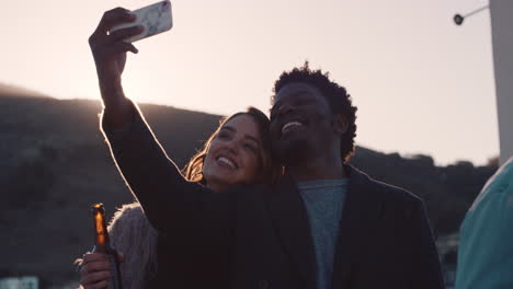 group-of-friends-hanging-out-together-enjoying-rooftop-party-at-sunset-taking-selfie-photos-using-smartphone-drinking-alcohol-having-fun-on-weekend-sharing-celebration