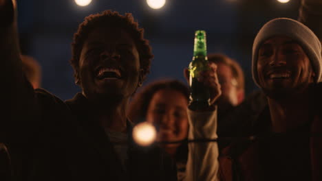 happy-rooftop-party-friends-having-fun-young-african-american-man-taking-photos-using-smartphone-sharing-weekend-lifestyle-on-social-media-at-night