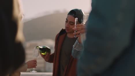 diverse-group-of-friends-celebrating-rooftop-party-drinking-alcohol-young-man-pouring-champagne-enjoying-reunion-celebration-at-sunset