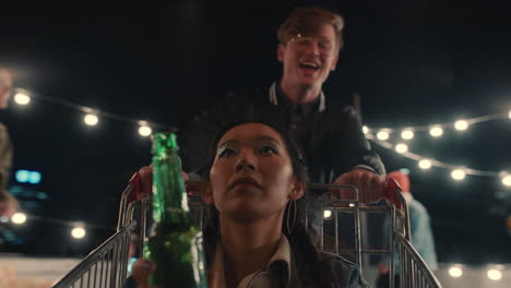 beautiful-asian-woman-having-fun-sitting-in-shopping-cart-group-of-friends-enjoying-crazy-rooftop-party-at-night-playfully-celebrating-weekend-drinking