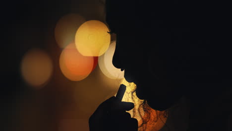 silhouette-of-woman-applying-lipstick-makeup-in-city-at-night-preparing-for-evening-party-with-bokeh-lights-in-background