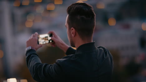 Junger-Mann-Fotografiert-Mit-Seinem-Smartphone-Die-Wunderschöne-Skyline-Der-Stadt-Und-Genießt-Den-Blick-Von-Der-Dachterrasse-Bei-Sonnenuntergang,-Indem-Er-Urlaubsfotos-In-Den-Sozialen-Medien-Teilt