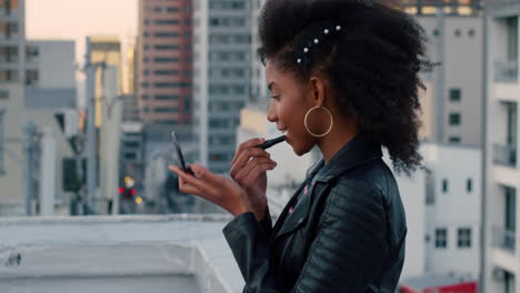 slow-motion-beautiful-young-african-american-woman-applying-lipstick-makeup-on-rooftop-preparing-for-glamorous-urban-party-wearing-stylish-fashion-in-city-at-sunset
