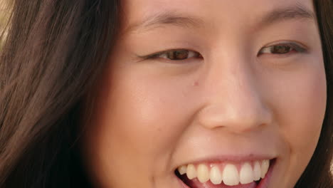 close-up-portrait-of-happy-asian-woman-smiling-enjoying-sunny-day-relaxing-on-summer-vacation-with-wind-blowing-hair