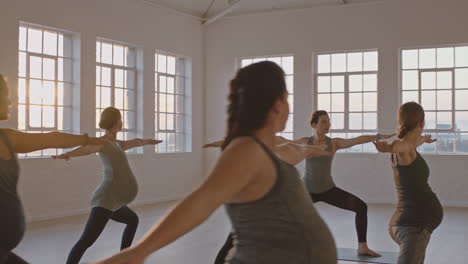 Yoga-Kurslehrer-Unterrichtet-Gesunde-Schwangere-Frauen,-Die-Kriegerpose-Praktizieren-Und-Bei-Sonnenaufgang-Gruppentraining-Im-Fitnessstudio-Genießen
