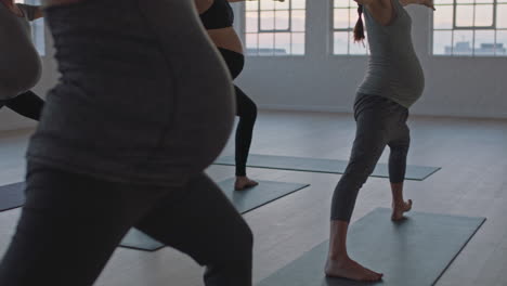 yoga-class-of-healthy-pregnant-women-practicing-warrior-pose-enjoying-group-physical-fitness-workout-with-instructor-in-studio-at-sunrise