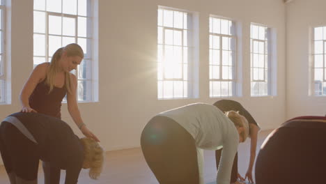 Yoga-Lehrerin-Unterrichtet-Reife-Frauen,-Indem-Sie-Bei-Sonnenaufgang-Im-Fitnessstudio-Die-Vorwärtsbeuge-Pose-Im-Stehen-übt-Und-Einen-Gesunden-Lebensstil-Genießt