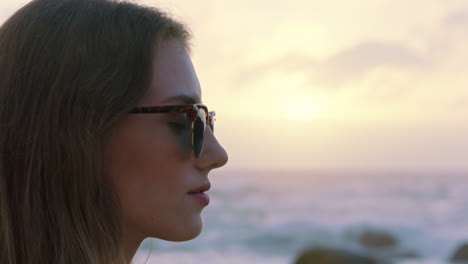 portrait-of-beautiful-woman-enjoying-calm-seaside-at-sunset-exploring-spirituality-looking-up-praying-contemplating-journey-relaxing-on-beach-wearing-sunglasses