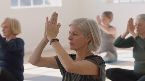 Yoga-Kurs,-Schöne-Alte-Frau,-Die-Gesunde-Meditation-Praktiziert,-Gebetshaltung-übt-Und-Das-Körperliche-Fitnesstraining-In-Der-Gruppe-Im-Studio-Genießt