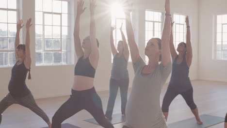 yoga-class-of-young-pregnant-women-practicing-warrior-pose-enjoying-healthy-lifestyle-group-fitness-workout-in-exercise-studio-at-sunrise